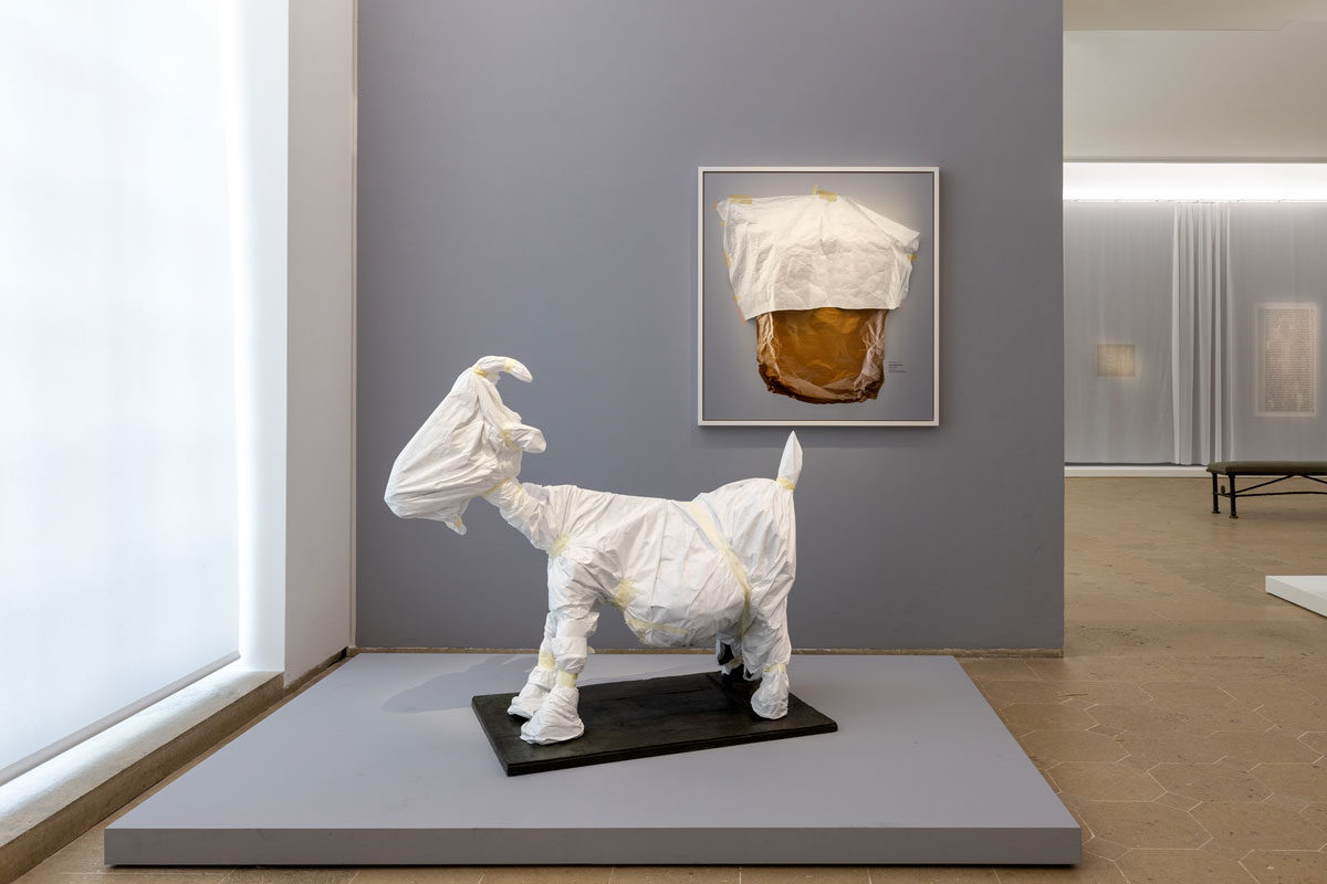 A sculpture of a goat wrapped in cloth, along with a painting on a wall that is also partially obscured by a cloth wrapping.