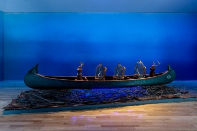 A sculptural installation showing a canoe on a bed of branches in a blue-painted room.