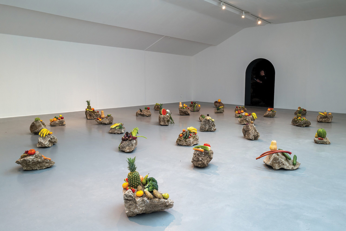 A group of stones arrayed around a gallery with fruits and vegetables laid on top of them.