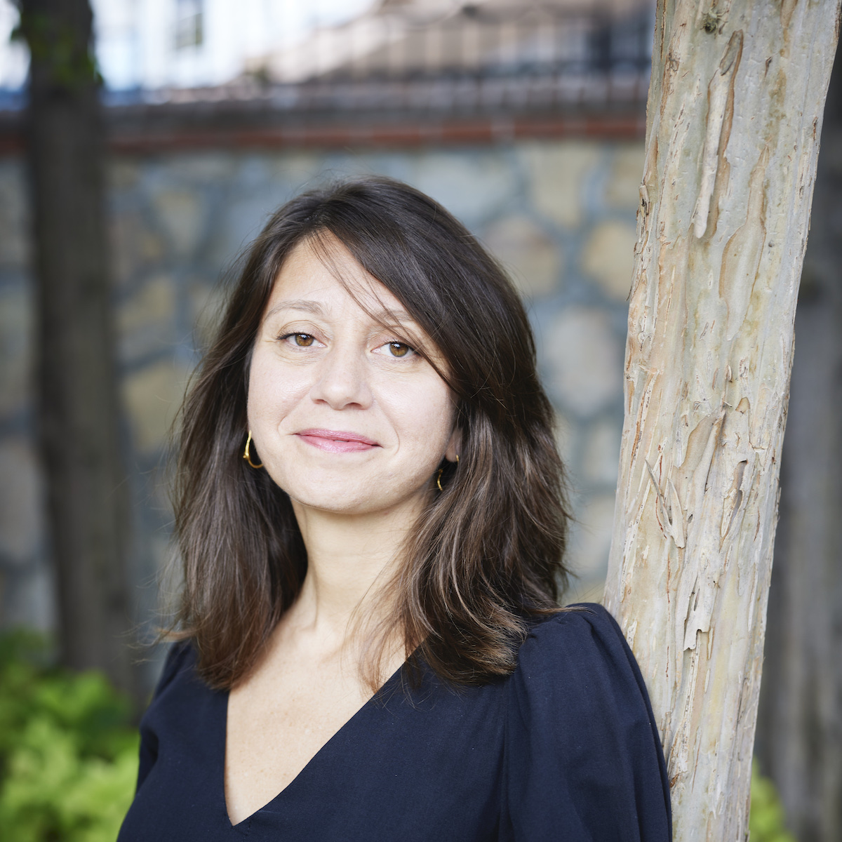 A smiling woman in a black shirt against a stone wall.