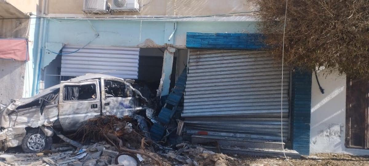 A smashed-up car in a building whose shutters have also been destroyed.