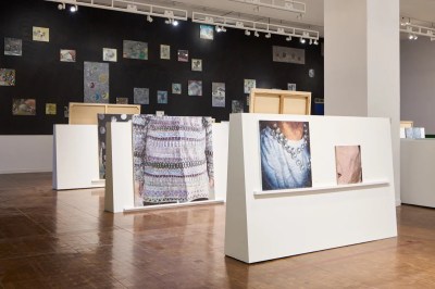 Images of close-ups of clothed bodies resting on ledges on white divider walls in a museum.