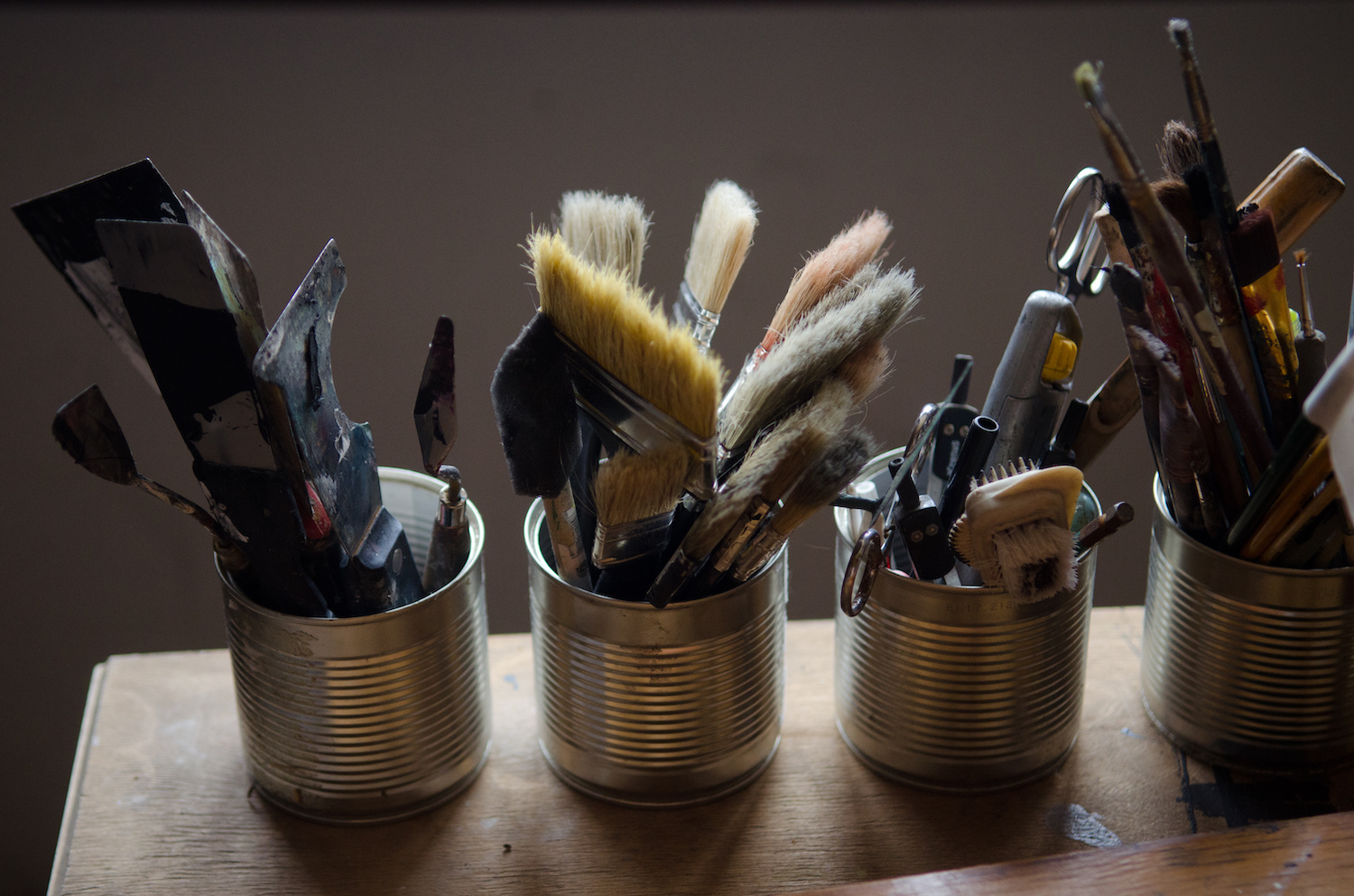 Brushes, pencils and other drawing tools are collected in three jars on the table in the artist's studio
