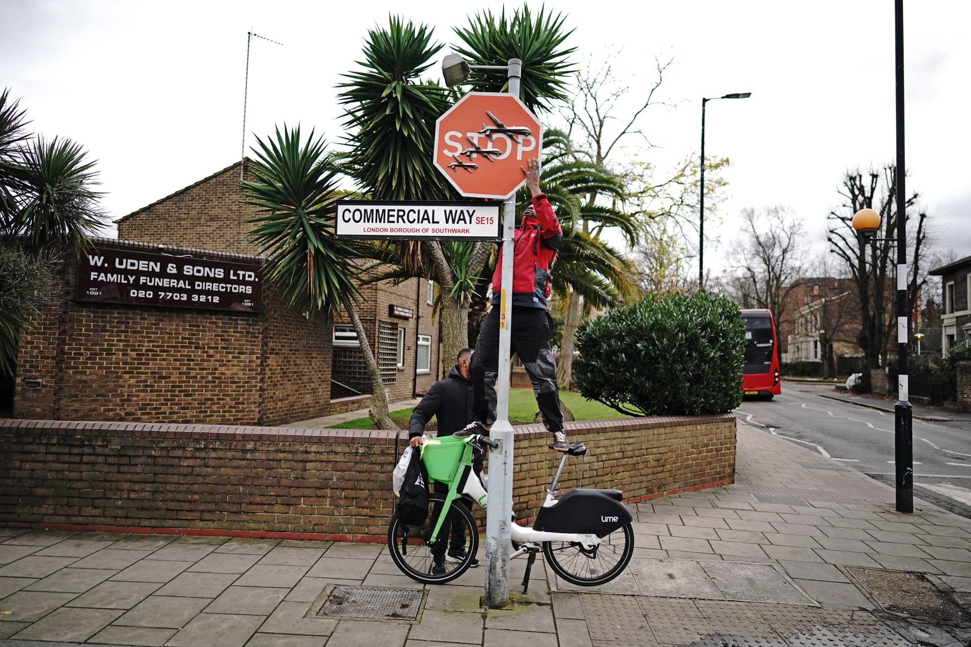 People remove a piece of art work by Banksy, which shows what looks like three drones on a traffic stop sign, which was unveiled at the intersection of Southampton Way and Commercial Way in Peckham, south east London. Picture date: Friday December 22, 2023.