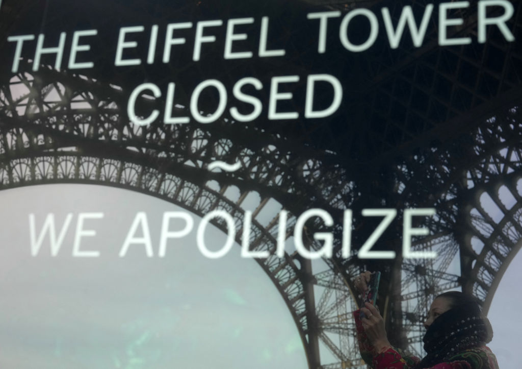 This photograph taken on December 27, 2023 in Paris shows the reflection of a tourist and the Eiffel Tower in a board informing visitors that the site is closed after staff went on strike. The strike on the 100th anniversary of the death of engineer Gustave Eiffel, who built the tower, was to protest about "the current way it is managed", the hard-left CGT union said in a statement. (Photo by Dimitar DILKOFF / AFP) (Photo by DIMITAR DILKOFF/AFP via Getty Images)
