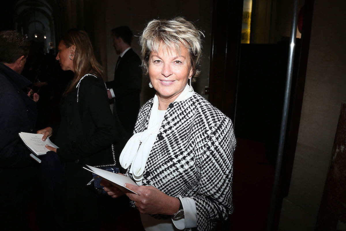 Portrait of Myriam Ullens smiling and holding a sheet of paper at a party.