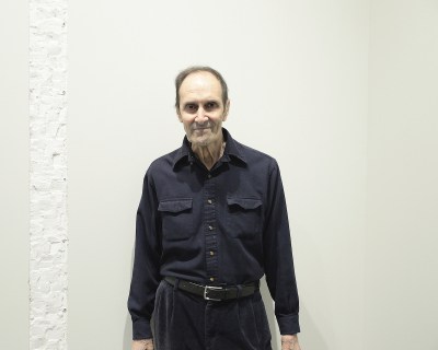 A man in a dark double-breasted shirt standing against a white wall.