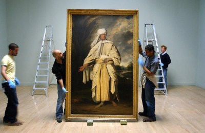 A group of installers holding a large painting of an Asian man pictured against a cloudy landscape.