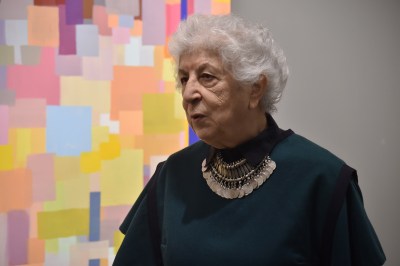 A woman standing beside an abstract painting showing many superimposed colorful squares.