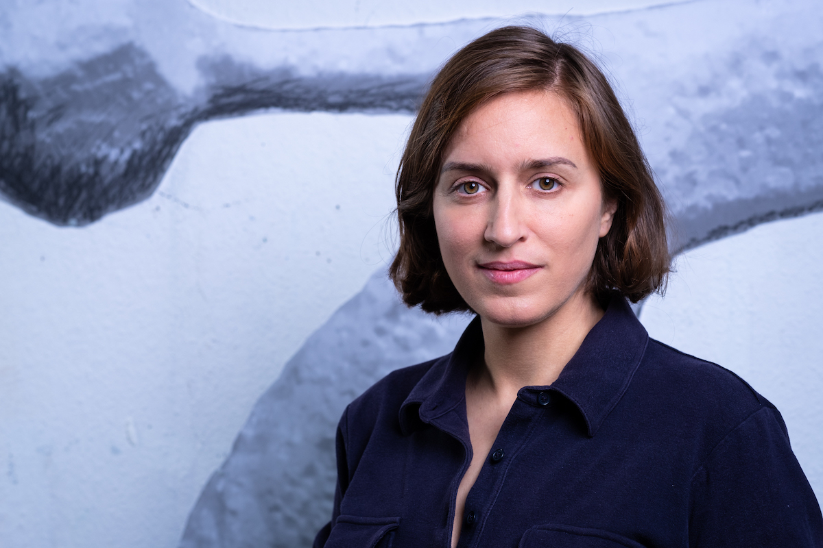 A woman with a bob standing in a blue wall.