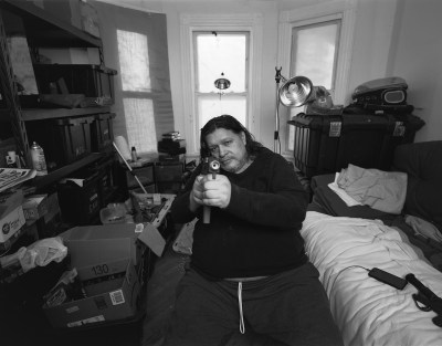 A man pointing a gun at the camera in a bedroom.