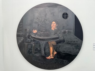 A round painting that is mostly black with a mother and child sitting at a table.
