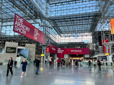Large glassed-in atrium with a line of people at an entrance to an art fair. Hanging above is a sign that says THE ARMORY SHOW.