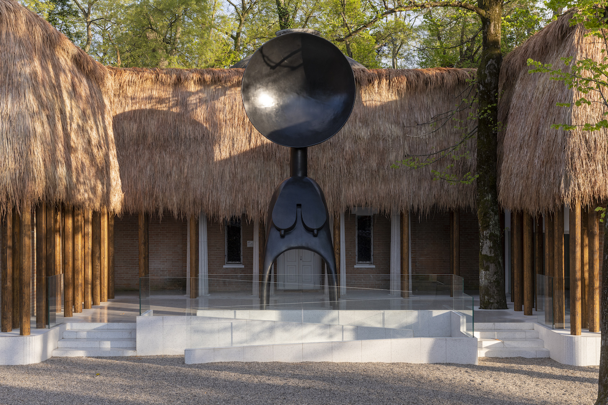 Thatched structure with a giant sculpture of a form with a spoon for a head.