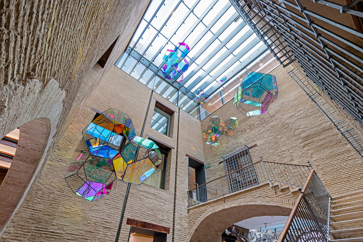 A wide open brick entrance hall from which hang four giant clusters of translucent glass bubbles.