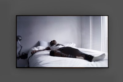 Image of a flat-screen showing a black-and-white video fo a person sleeping.